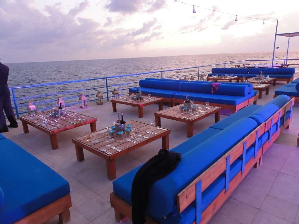 A dinner set up on the terrace at Sporting Club Beach at sunset, daybeds and laid tables