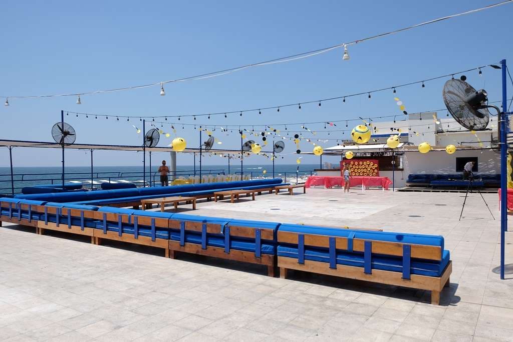 A daytime event set up on the terrace at Sporting Club Beach, bench seating and bright décor