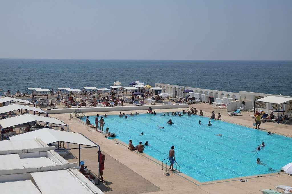 Swimmers and loungers on the pool deck at Sporting Club Beach, the Mediterranean behind