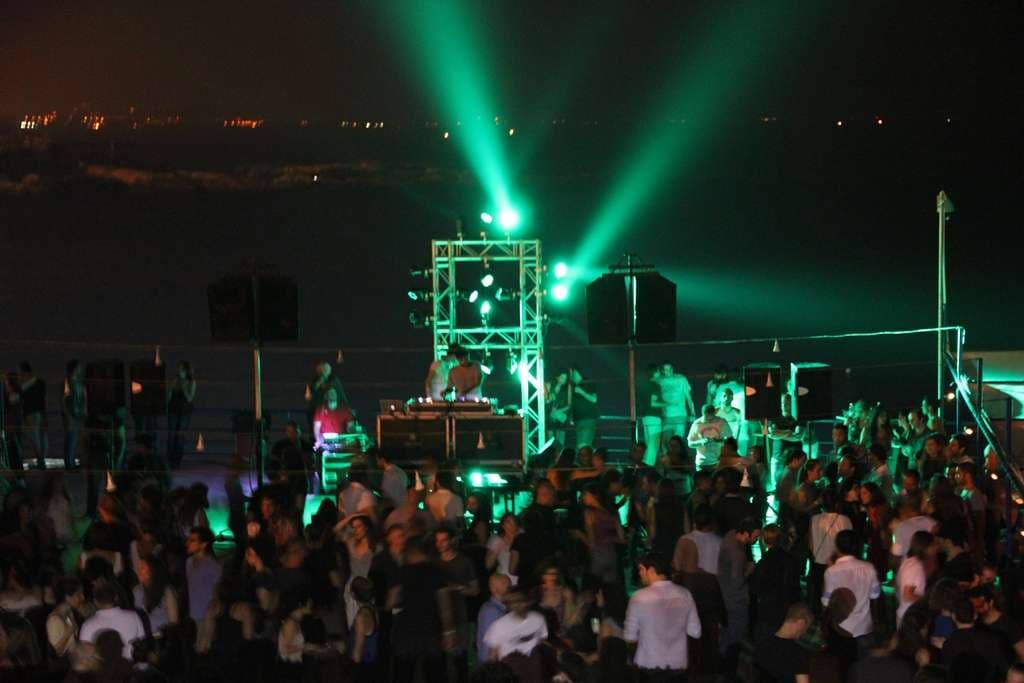 A night party with green stage lighting and a DJ on the open-air terrace at Sporting Club Beach, Ras Beirut