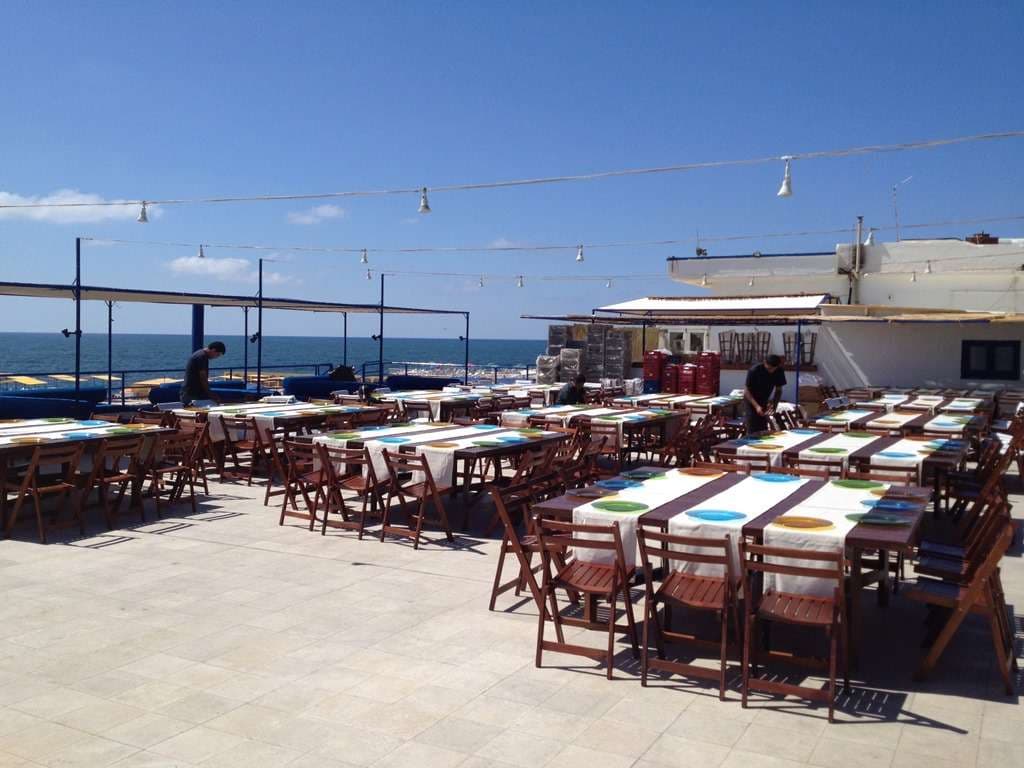 Tables laid for a large lunch on the seaside terrace under string lights at Sporting Club Beach, Ras Beirut