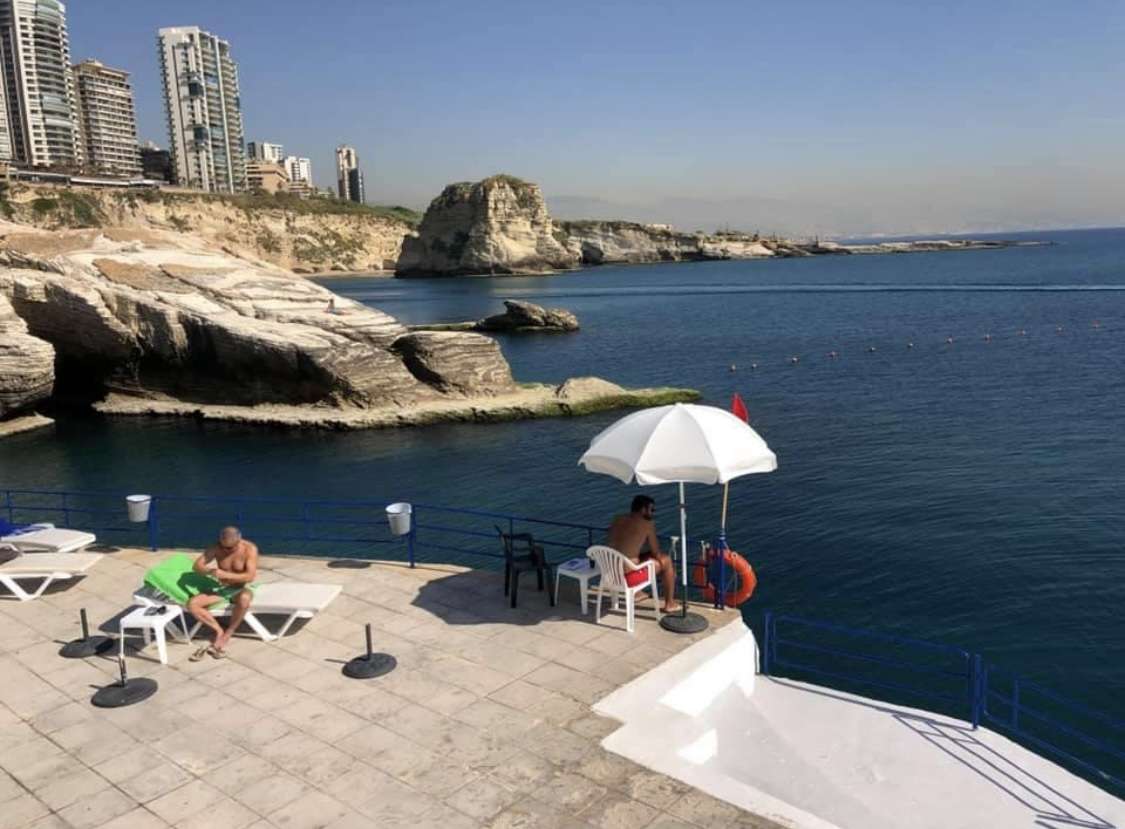 Sunbathers on the rocky shoreline at Sporting Club Beach beside the Mediterranean