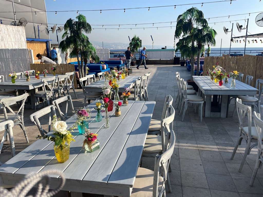 Long tables dressed with wildflowers and string lights for an event on the seaside terrace at Sporting Club Beach, Ras Beirut