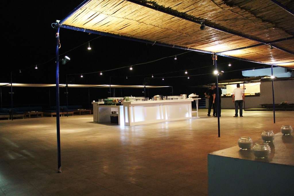 The event terrace at night with a long white bar under a reed-roof canopy at Sporting Club Beach