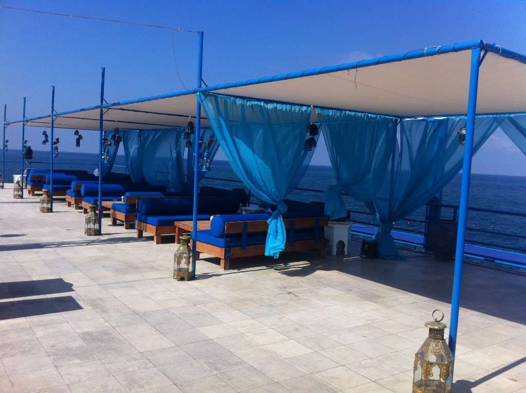 Daybeds with blue cushions and sheer drapes facing the open sea at Sporting Club Beach, Ras Beirut