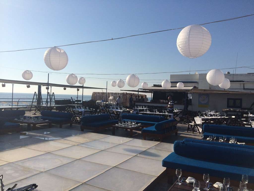 A seafront terrace set for dinner under paper lanterns at sunset at Sporting Club Beach, Ras Beirut