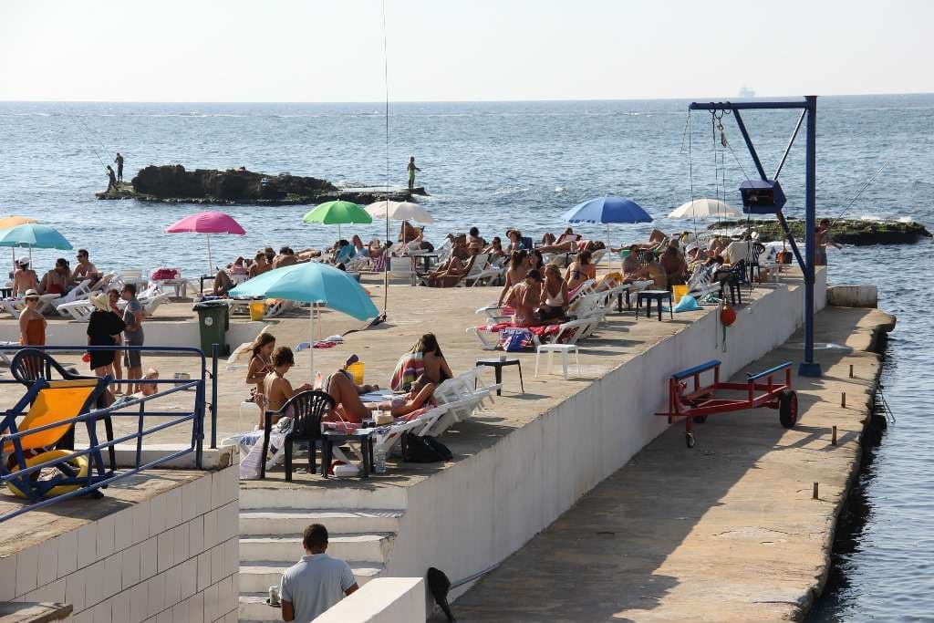 Swimmers diving into the sea from the rocks as waves break at Sporting Club Beach, Ras Beirut