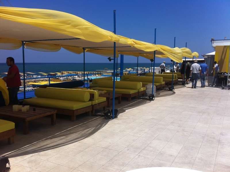 Daybeds and canopies being set up on the terrace above the sea at Sporting Club Beach