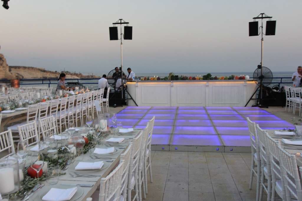 A lit dancefloor beside banquet tables and a seaside bar at dusk at Sporting Club Beach, Ras Beirut