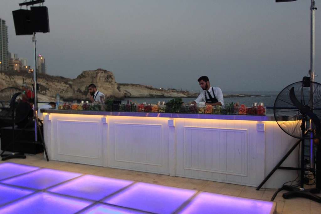 Bartenders at a lit seaside bar above the dancefloor at dusk at Sporting Club Beach, Ras Beirut