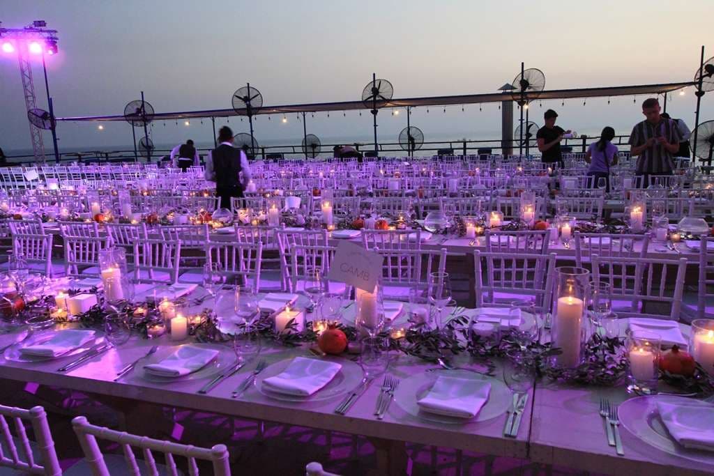 Candlelit banquet tables laid across a seafront event terrace at dusk at Sporting Club Beach, Ras Beirut