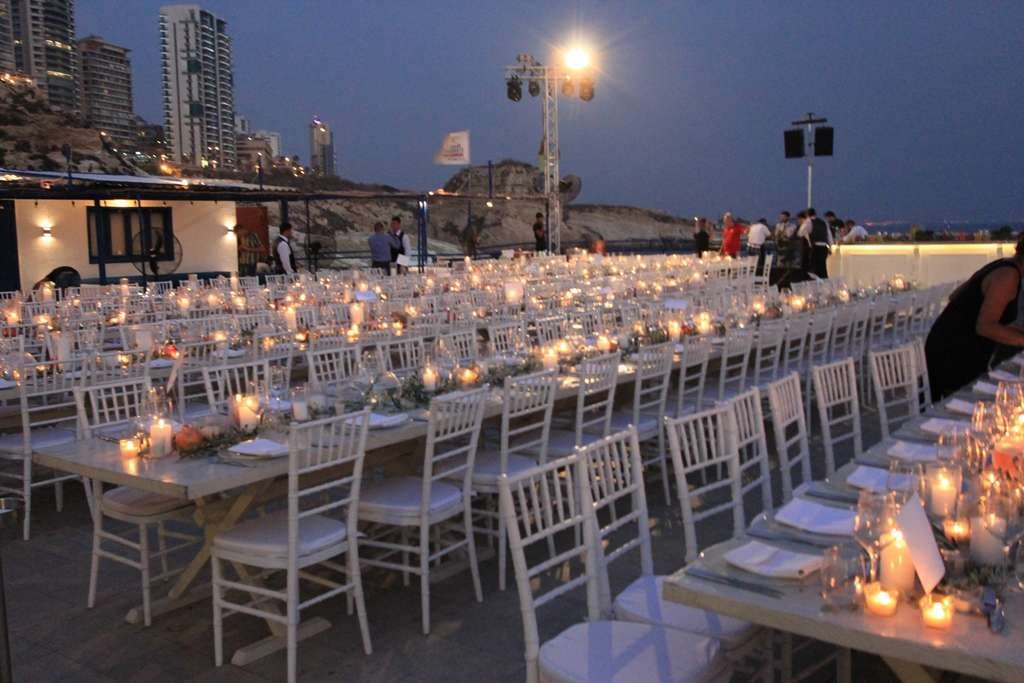 An evening event set with candlelit tables on the terrace overlooking the Beirut coastline at Sporting Club Beach