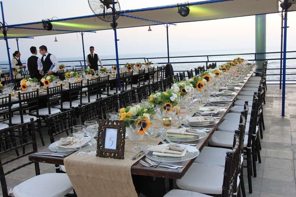 An event terrace with sunflower table settings and string lights overlooking the coastline at Sporting Club Beach, Ras Beirut