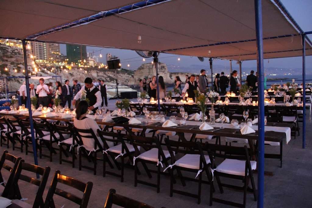 Guests dining at a long candlelit table on the seafront terrace at dusk at Sporting Club Beach, Ras Beirut