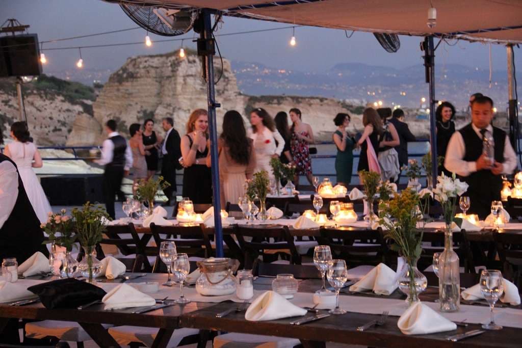 An evening event set under shade canopies with the Beirut skyline and coastline behind at Sporting Club Beach, Ras Beirut