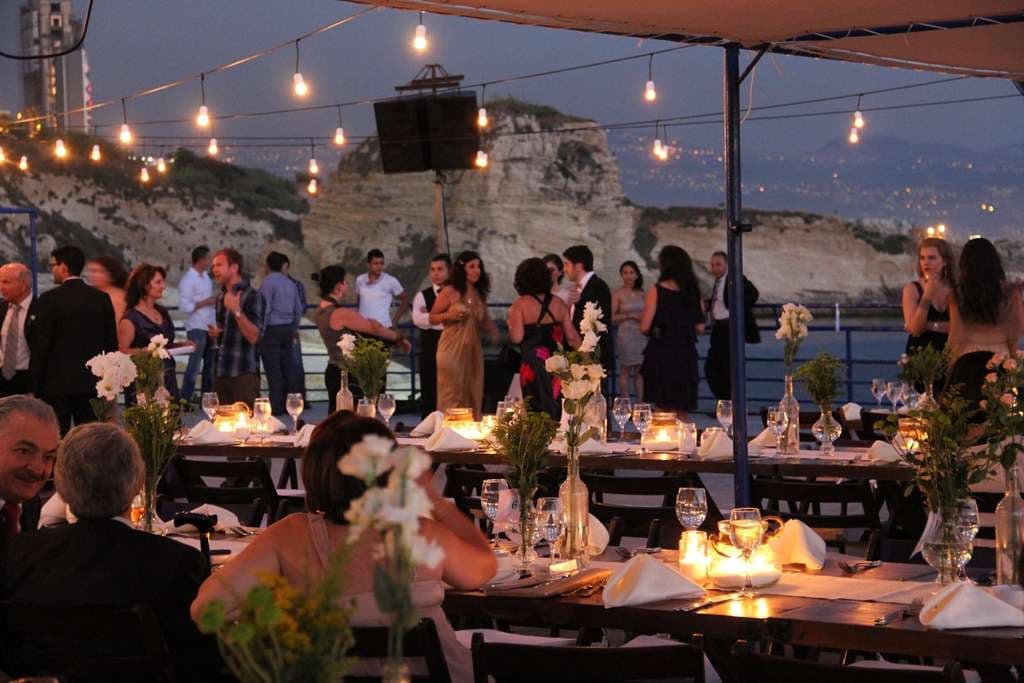 Guests at an evening event with set tables and cliffside views under string lights at Sporting Club Beach, Ras Beirut