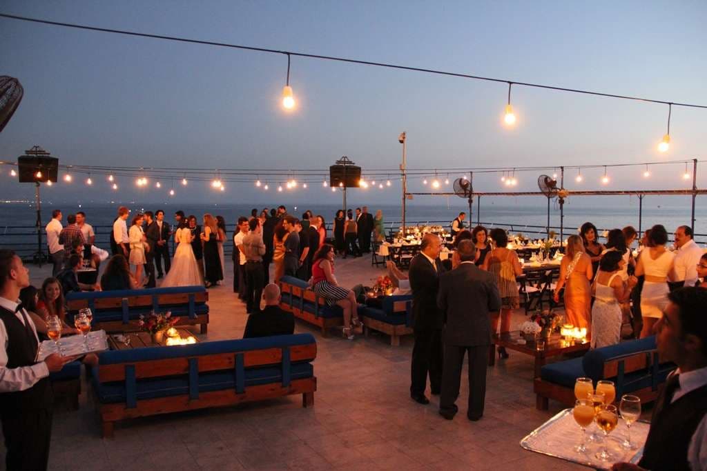 Guests gathered on the terrace under string lights at an evening event beside the sea at Sporting Club Beach, Ras Beirut