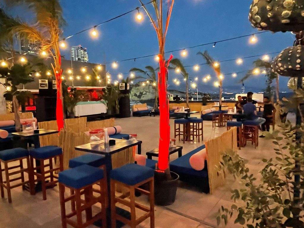 An open-air bar terrace with blue seating and string lights at dusk at Sporting Club Beach, Ras Beirut
