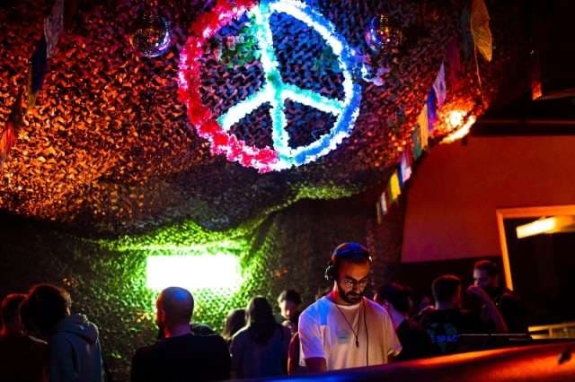A DJ playing under the lit peace-sign installation at The Loft by Sporting, Sporting Club Beach