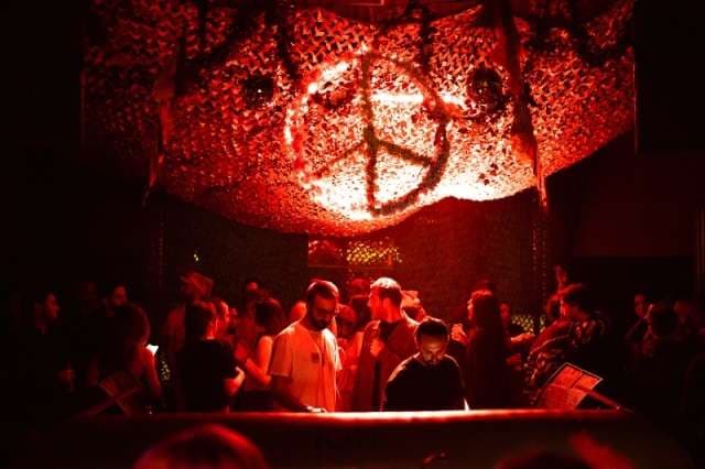 A crowd in red light beneath the peace-sign installation at The Loft by Sporting, Sporting Club Beach