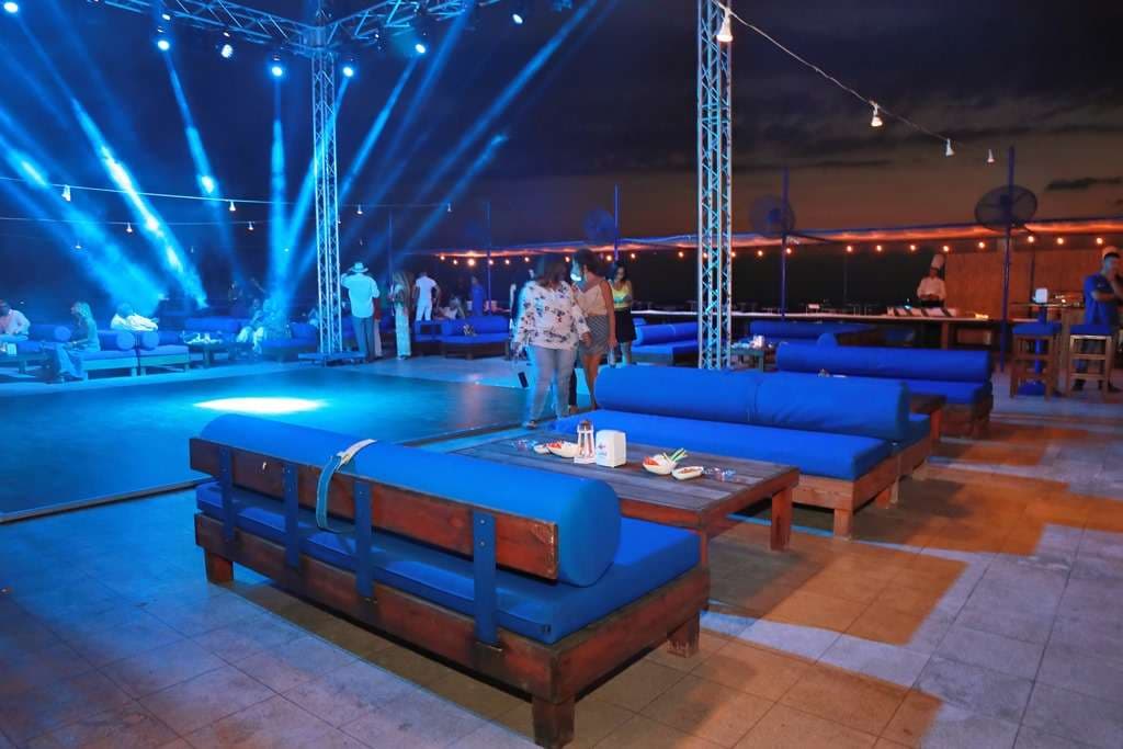 An open-air evening lounge with stage lighting beside the sea at Sporting Club Beach
