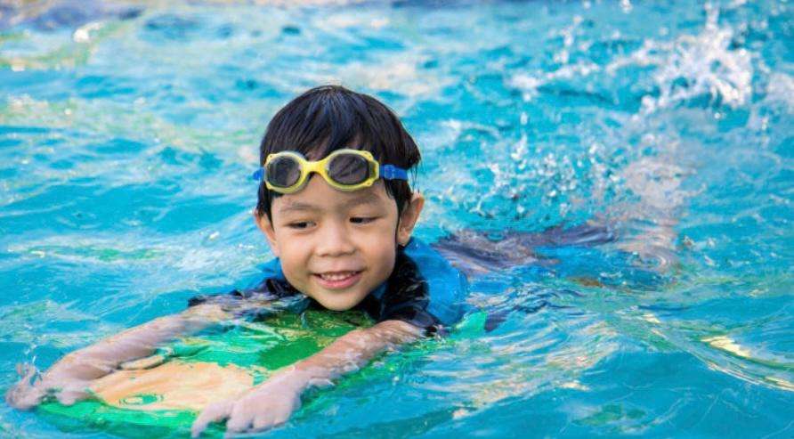 A child learning to swim with a kickboard at Sporting Club Beach