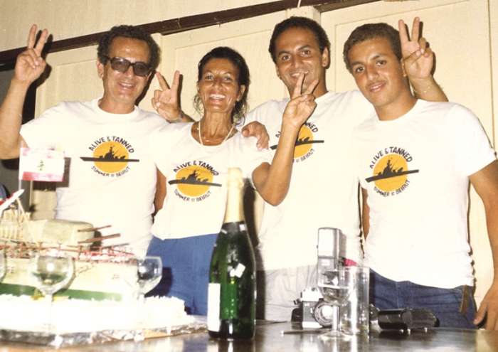 Four people in matching summer T-shirts behind a cake at Sporting Club Beach — an archive photograph