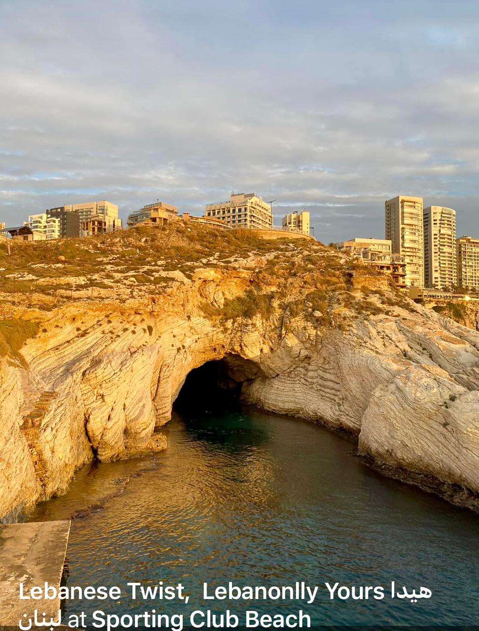 A sea cave in the rocky coastline with Beirut buildings above at Sporting Club Beach, Ras Beirut