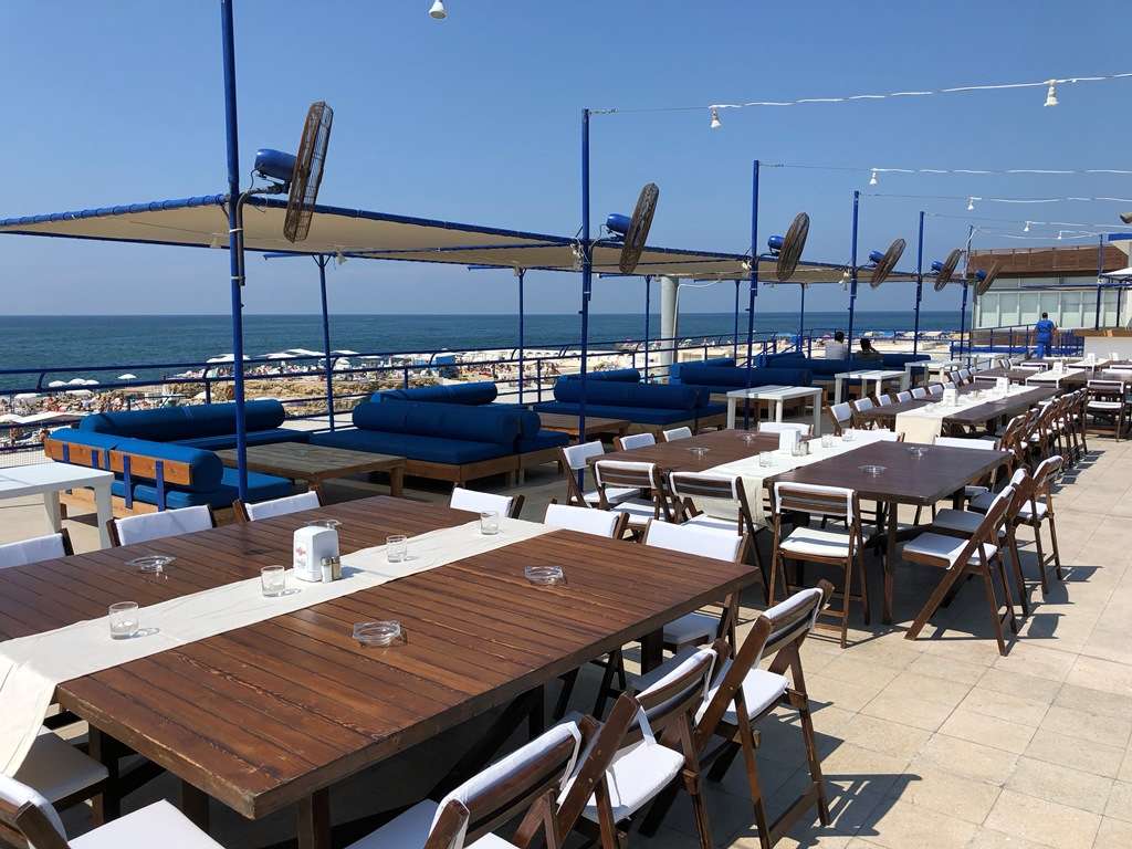 Guests at an evening event with set tables and the rocky coast behind at Sporting Club Beach