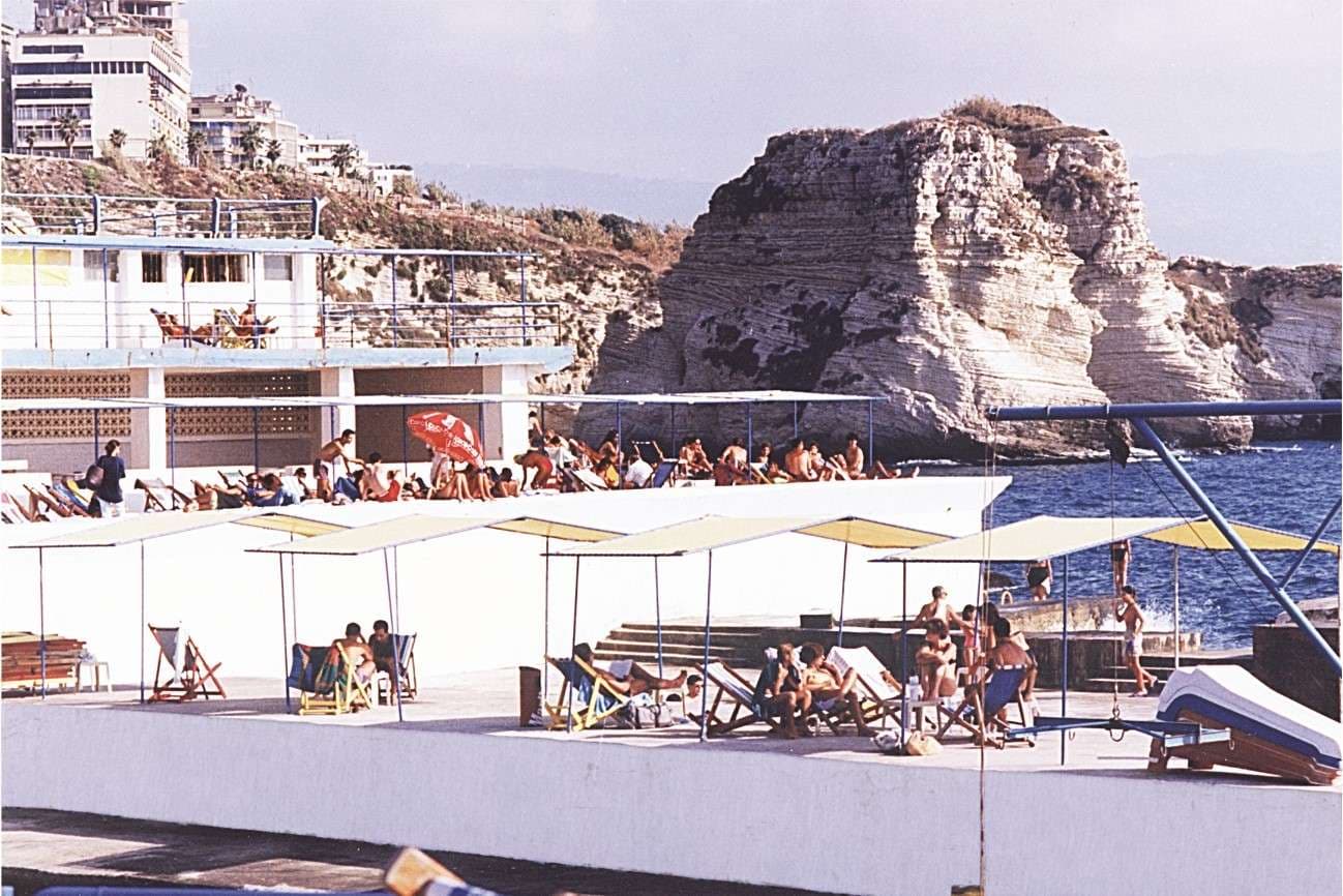 Sunbathers under parasols on the deck with the Pigeon Rocks behind at Sporting Club Beach — an archive photograph