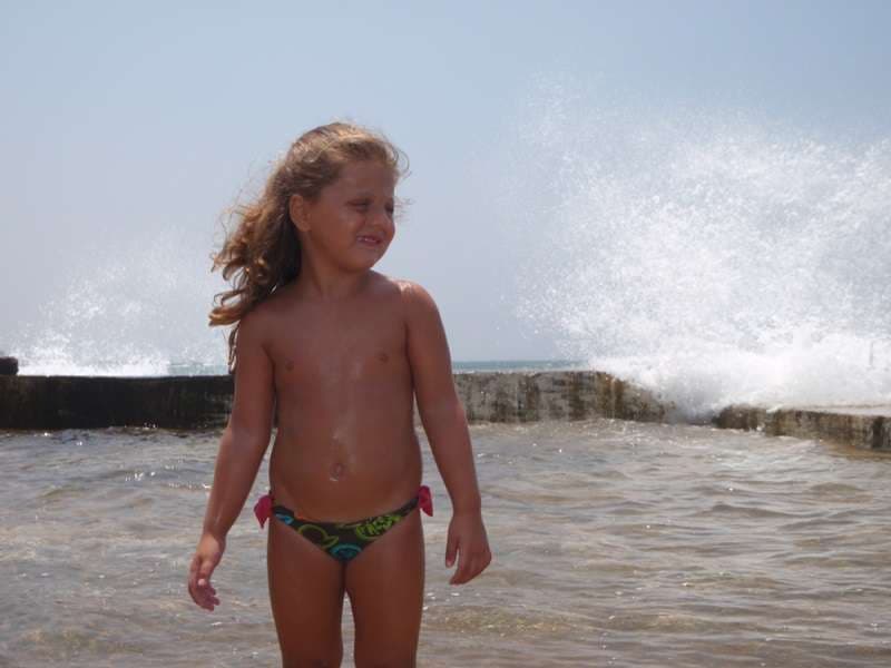 A child in the shallows as waves break over the sea wall at Sporting Club Beach, Ras Beirut
