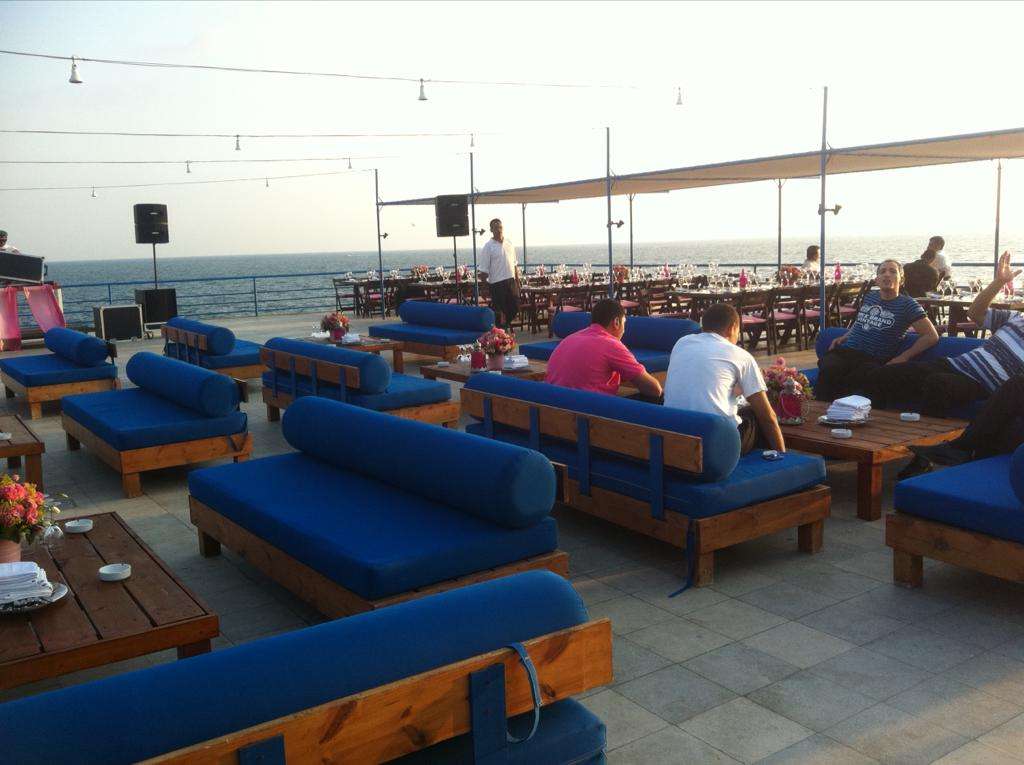 Blue lounge seating and dining tables set up on the seafront terrace at Sporting Club Beach