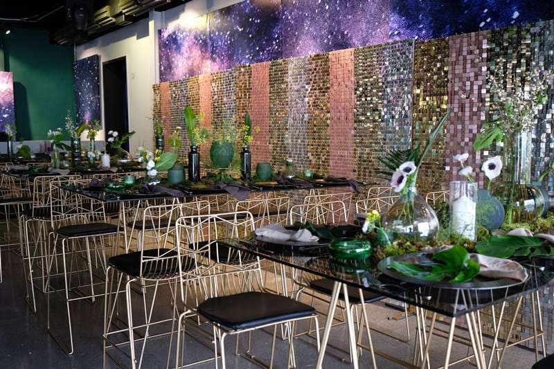 Tables set with a sequin backdrop and greenery for an event inside The Loft at Sporting Club Beach