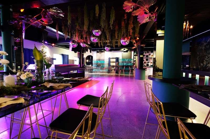 The Loft set with high tables, disco balls and hanging greenery under purple light at Sporting Club Beach