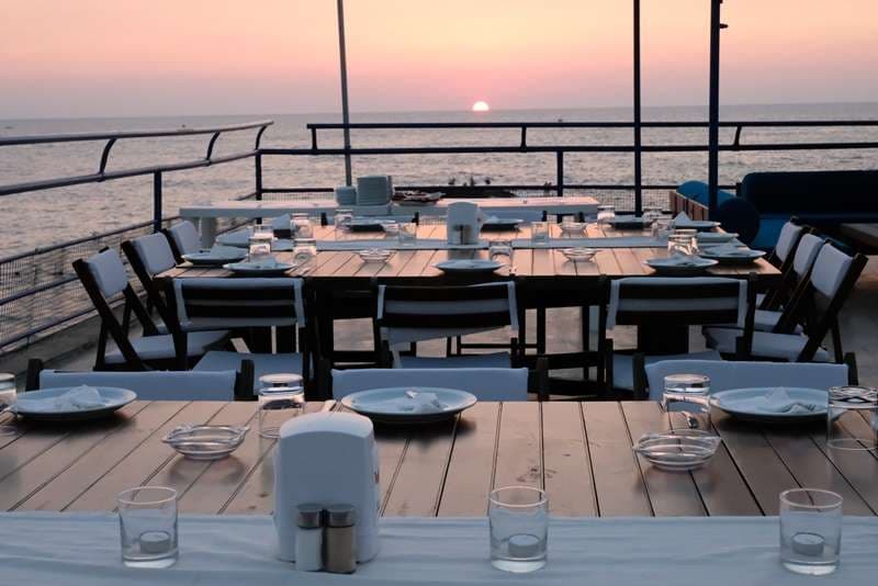 A set dining table on the deck facing the sea at sunset at Sporting Club Beach, Ras Beirut