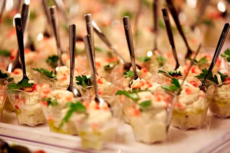 Individual cups of dip topped with parsley and red garnish, with spoons, at Sporting Club Beach