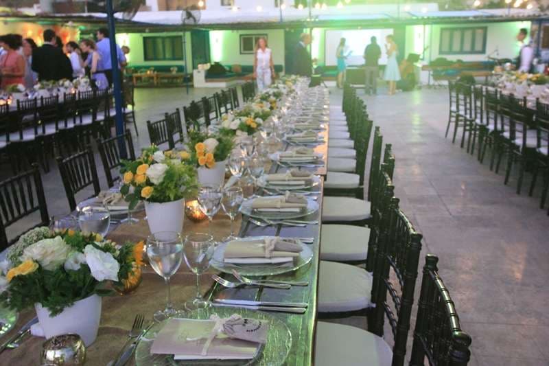 An outdoor banquet with long tables, floral centrepieces and green lighting at Sporting Club Beach