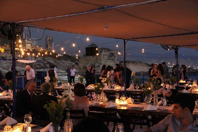 An outdoor evening banquet under canopy with the coastline behind at Sporting Club Beach