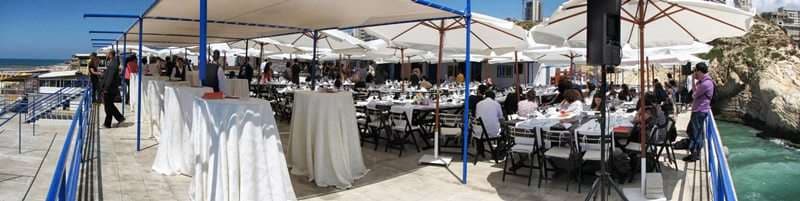A seaside event under white umbrellas with seated guests at Sporting Club Beach