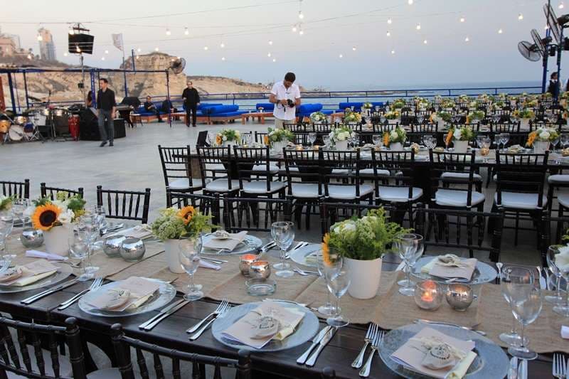 Outdoor terrace dinner tables set with plates and flowers beside the sea at Sporting Club Beach