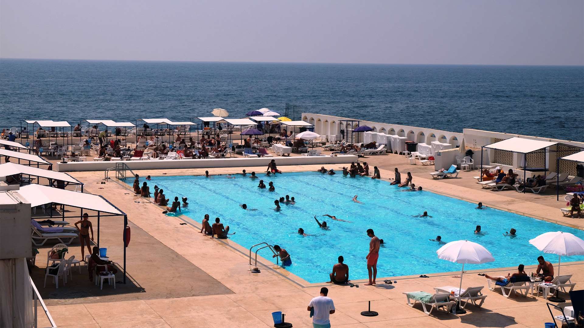 The saltwater pools and terraces at Sporting Club Beach, seen from above with the Mediterranean beyond